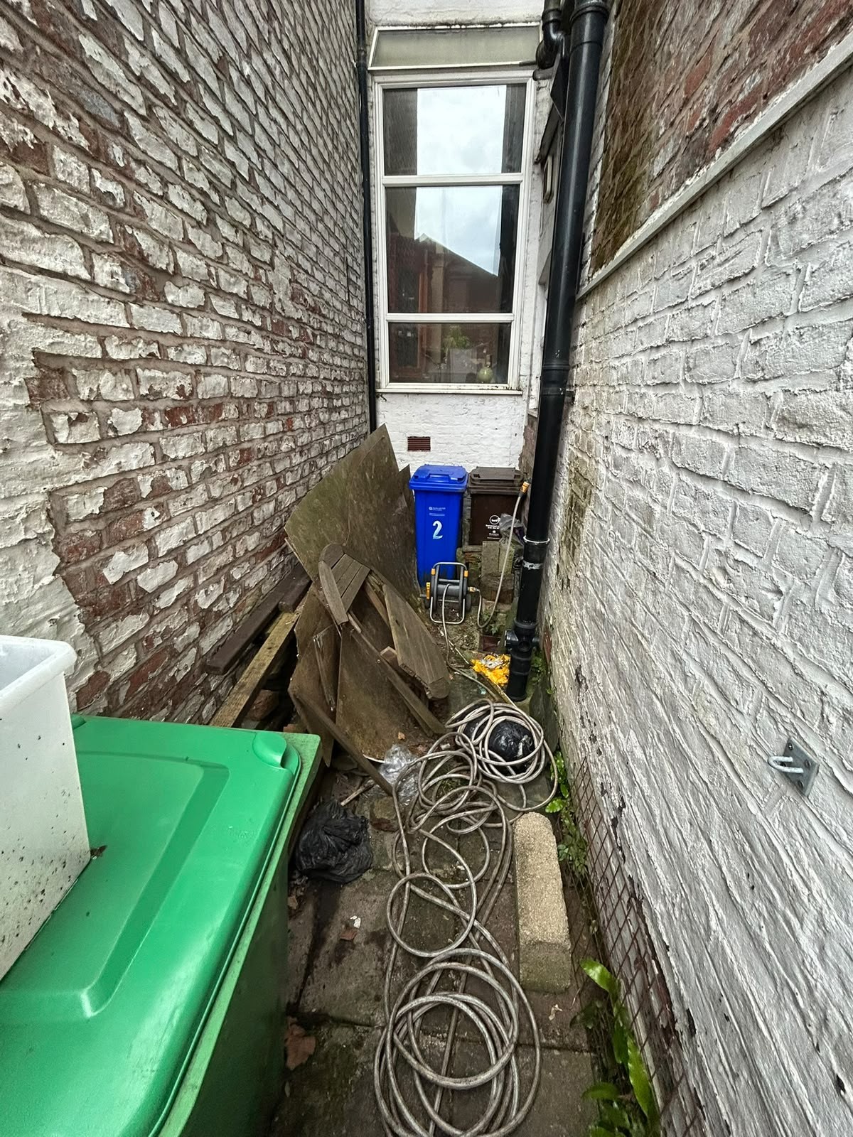 Before rubbish removal: narrow rear passage of a terraced property blocked with timber boards, coiled cable and general waste