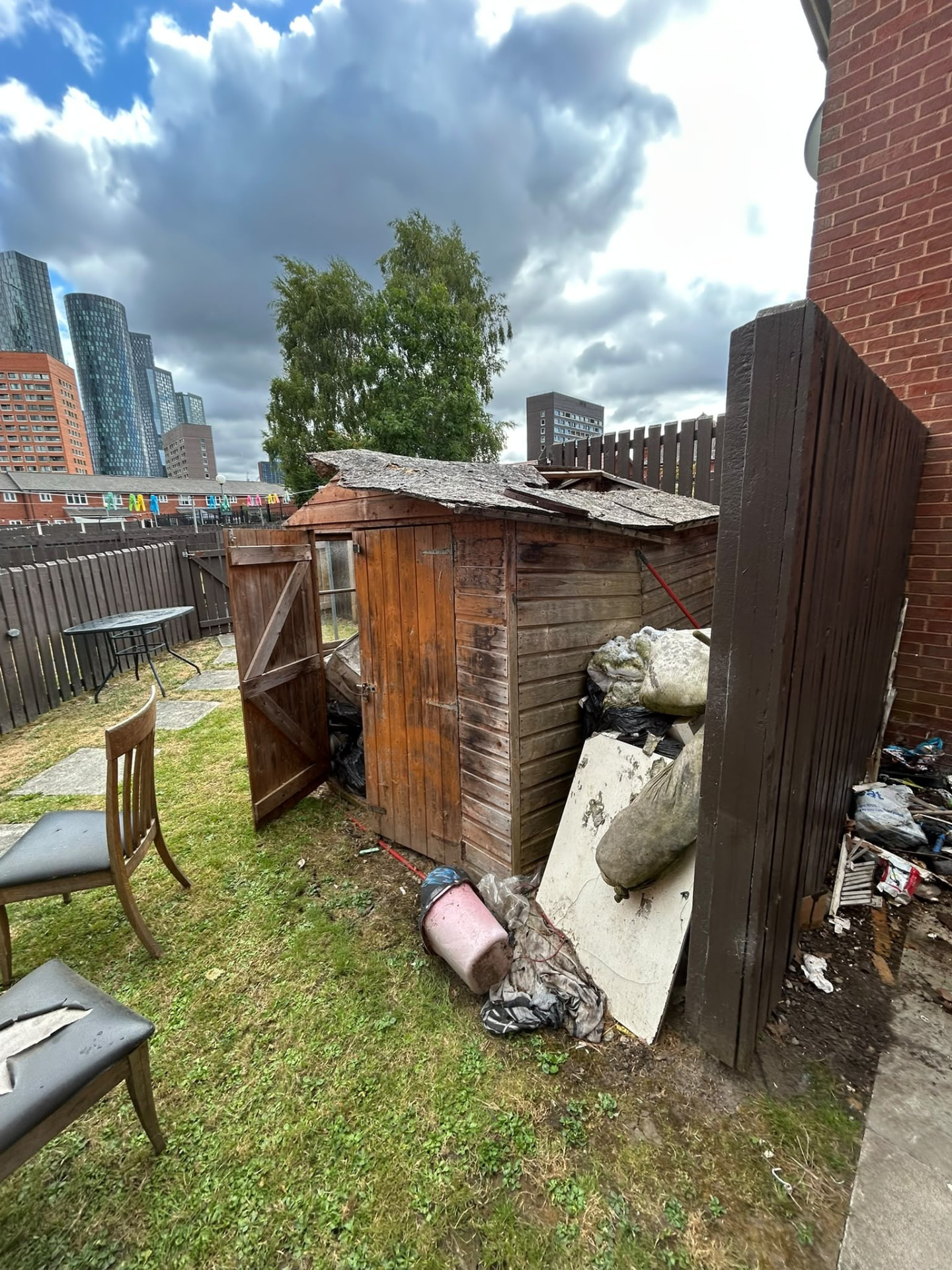 Overgrown Manchester garden with a collapsing shed, rubbish and dumped furniture before green waste clearance