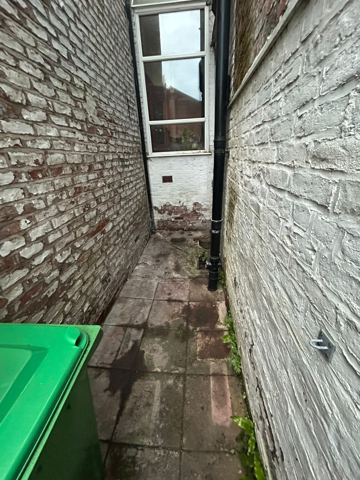 After rubbish removal: the same rear passage cleared to bare flags with unobstructed access to the back door and bin