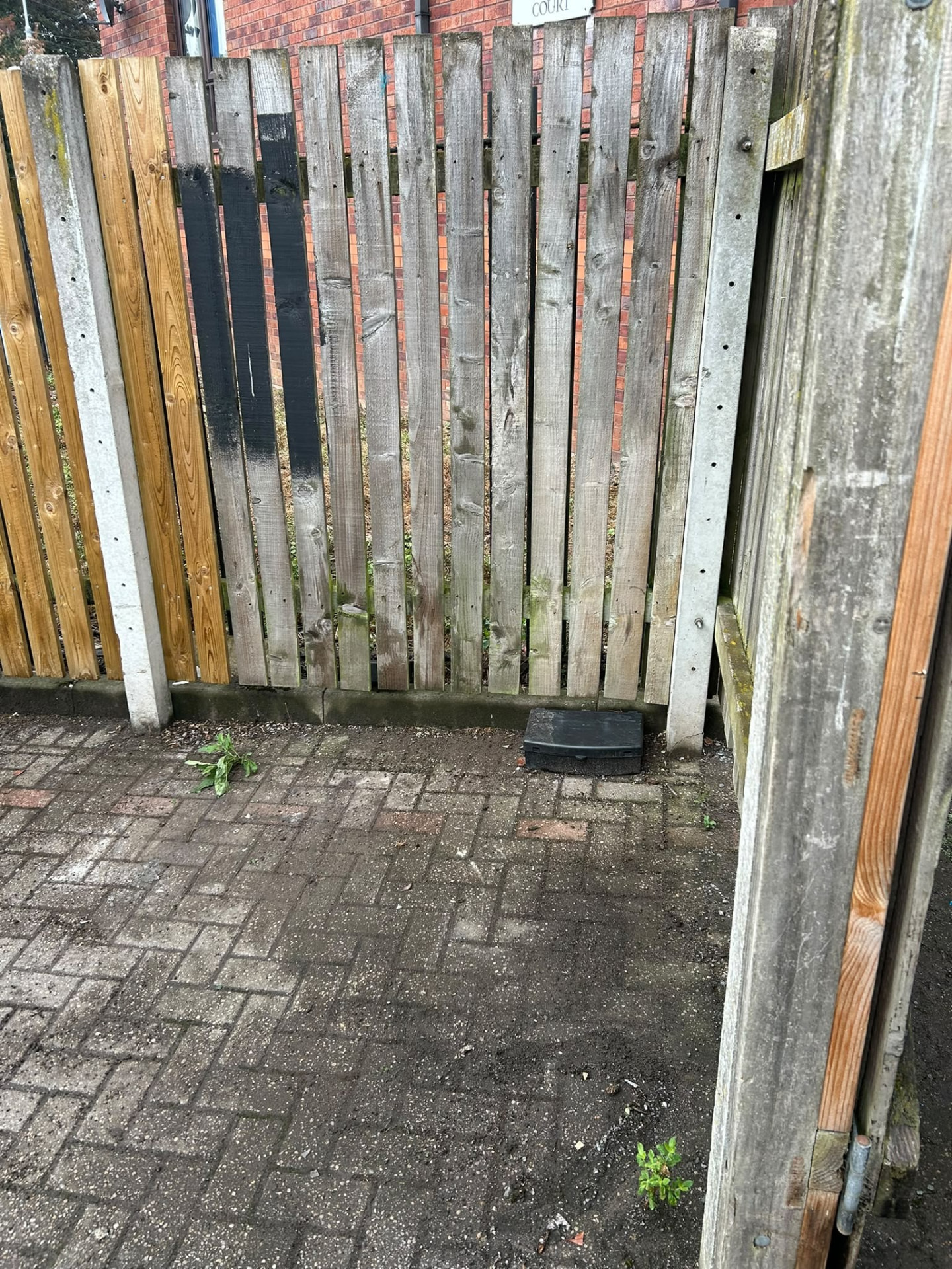 Paved bin area beside a timber fence swept clean after a bin shed clearance in Manchester