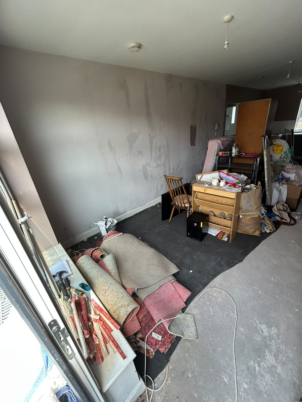 Before flat clearance: living space cluttered with rolled carpets, furniture, boxes and household items left after a tenancy