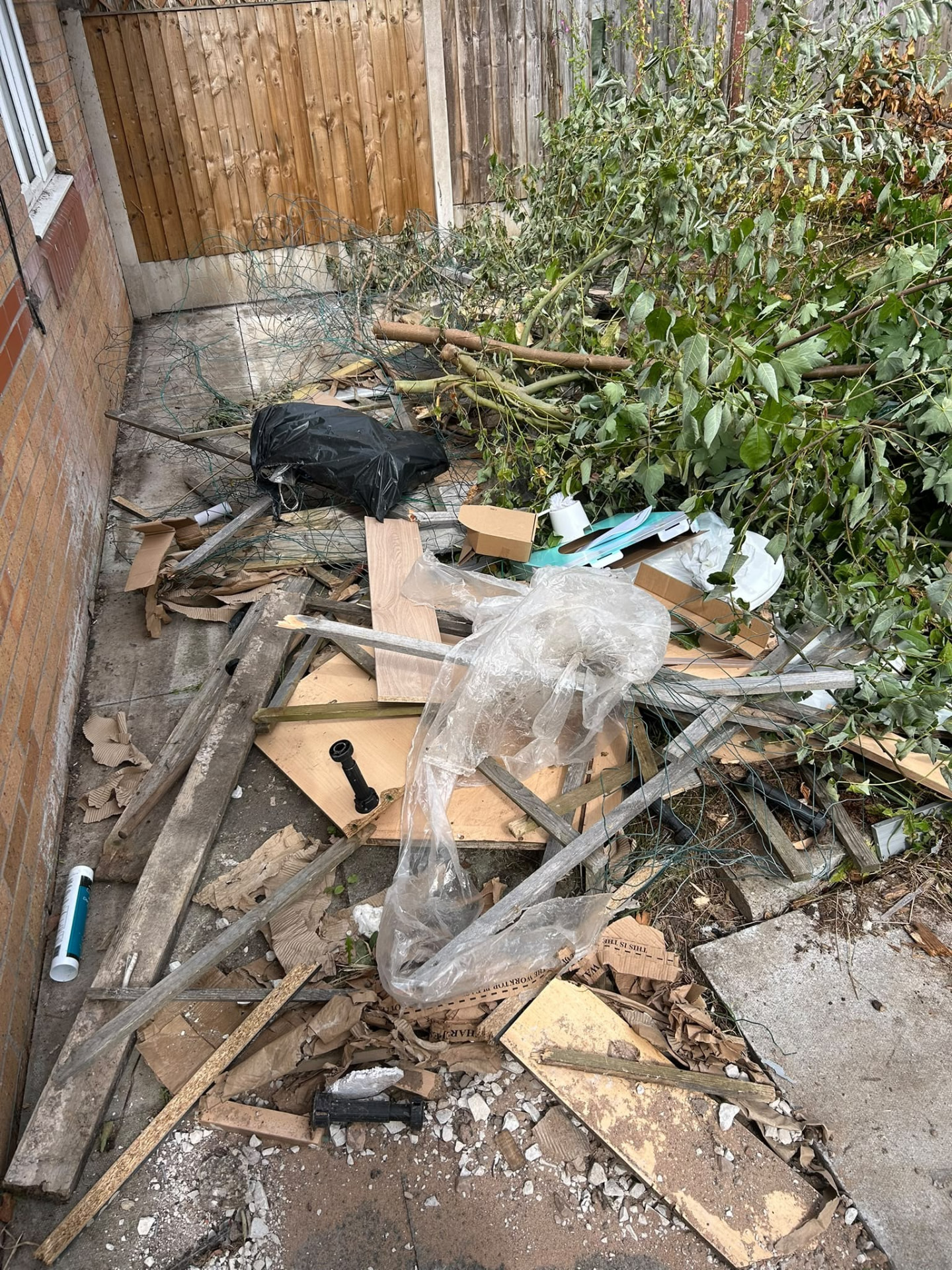 Narrow Manchester garden passage piled with cut branches, timber and rubble ready for green waste removal