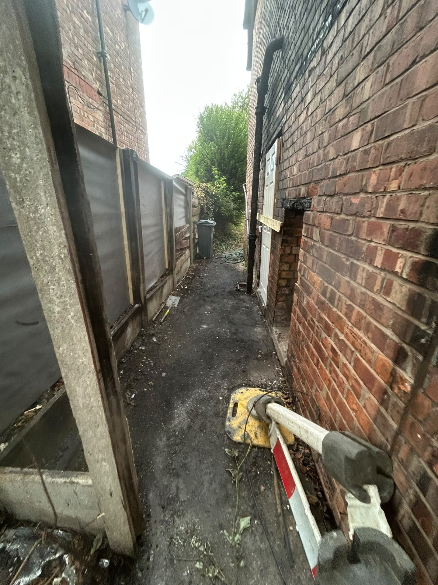 Narrow Manchester alleyway cleared of rubbish during a waste removal job, with tools left ready